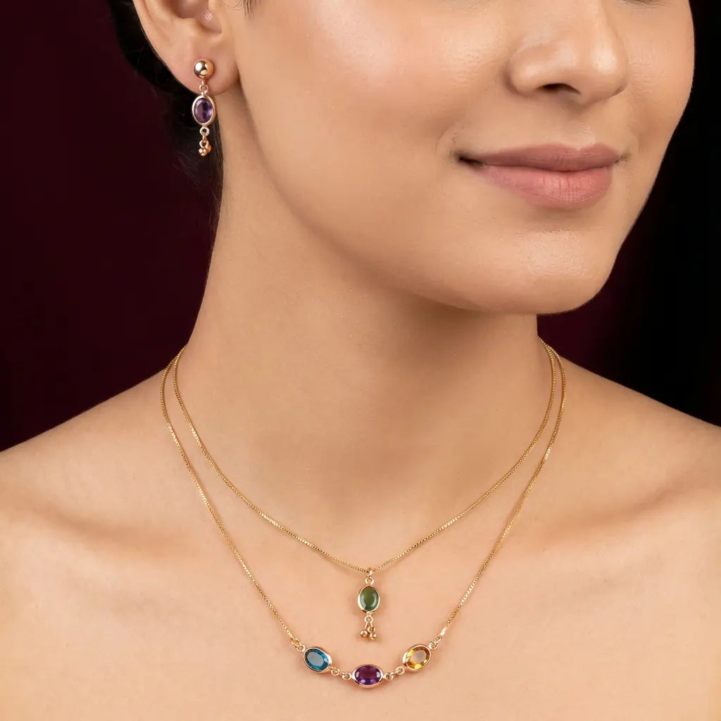 Close-up of a woman wearing a gold necklace with colorful gemstones and matching earrings.