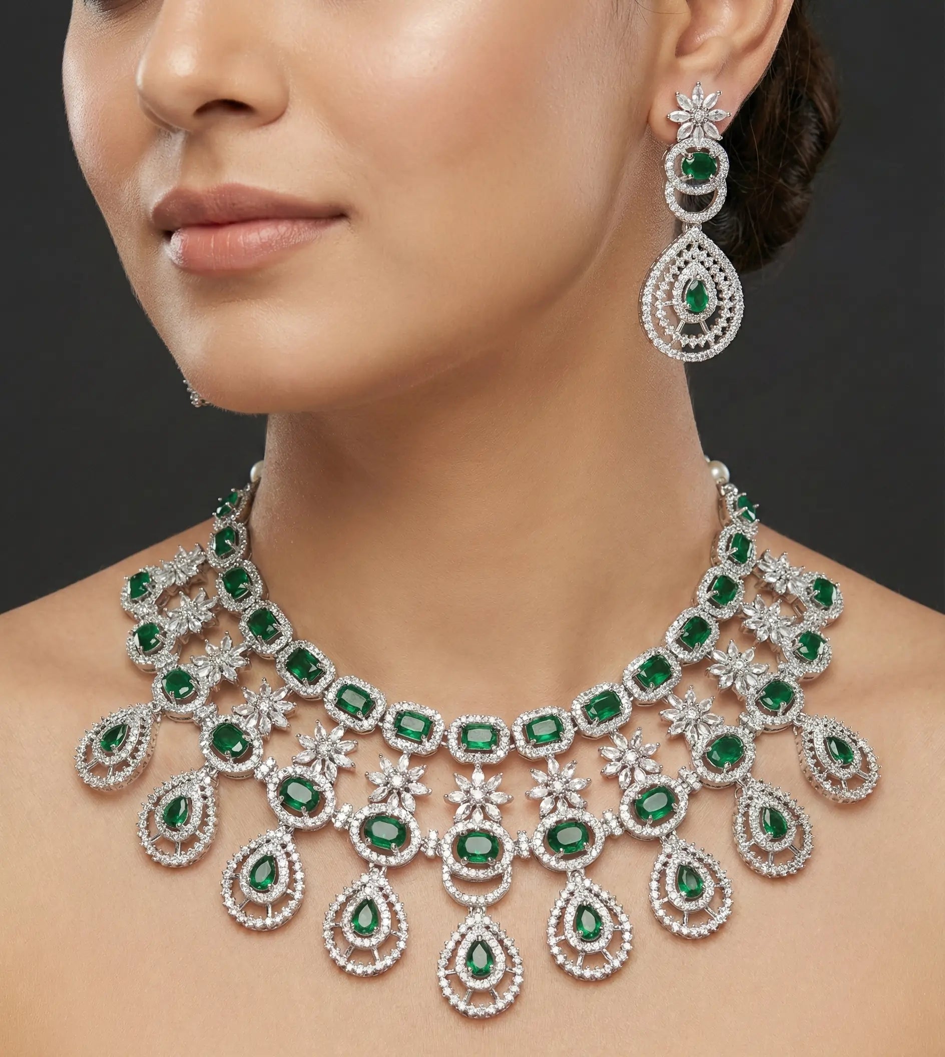 Woman wearing a luxurious emerald and diamond necklace and earrings on a dark background