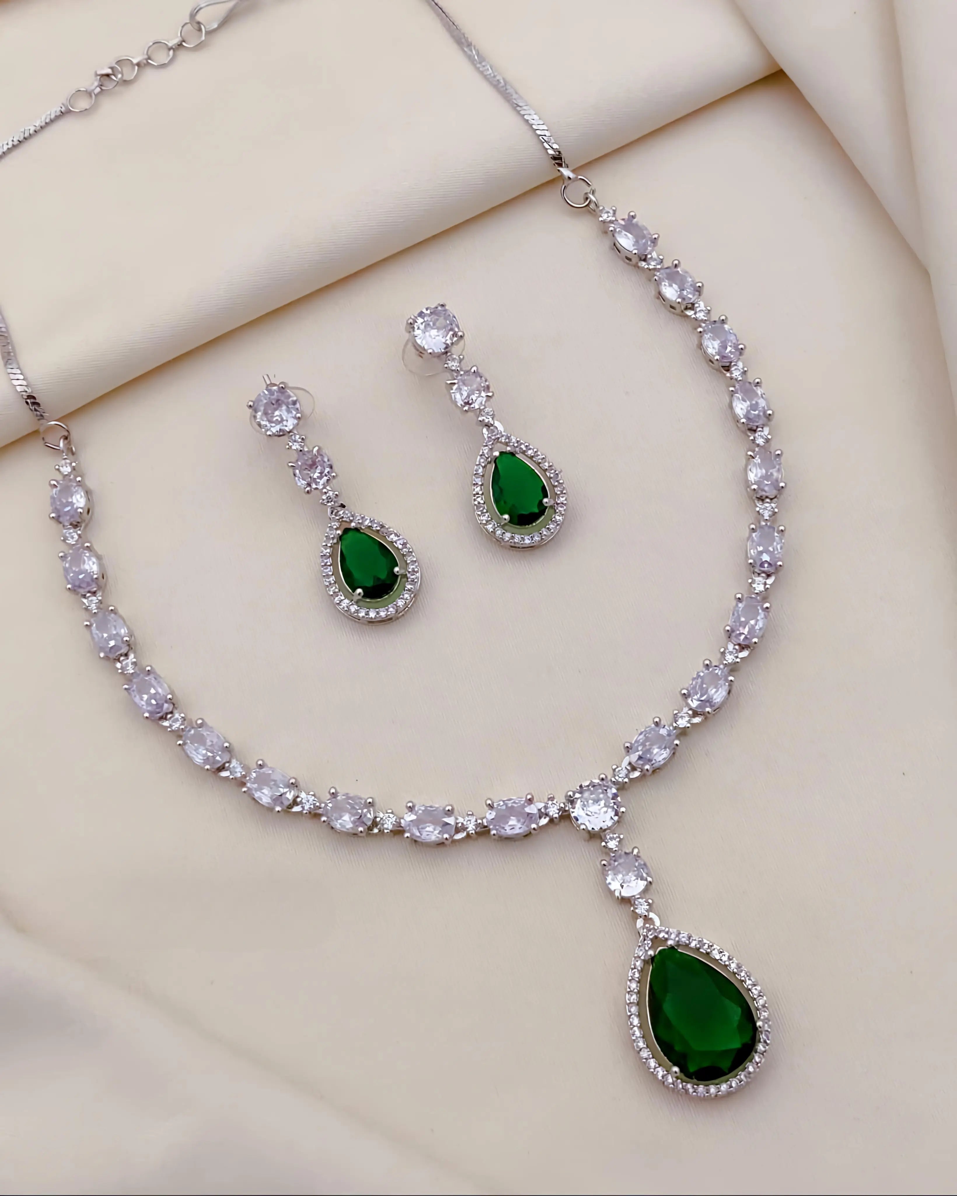 Jewelry set with necklace and earrings featuring green gemstones on a beige background