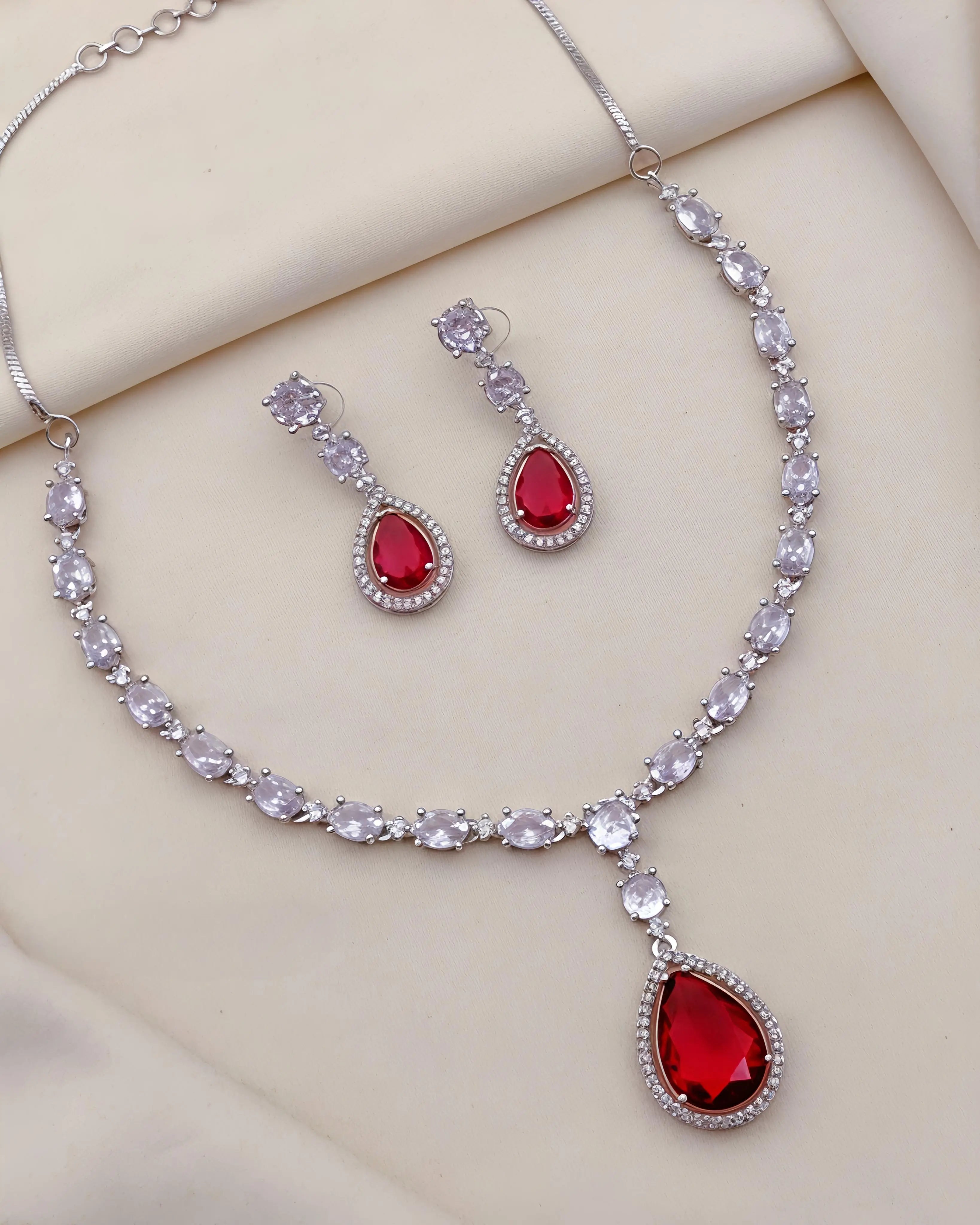 Jewelry set with red teardrop stones on a beige background